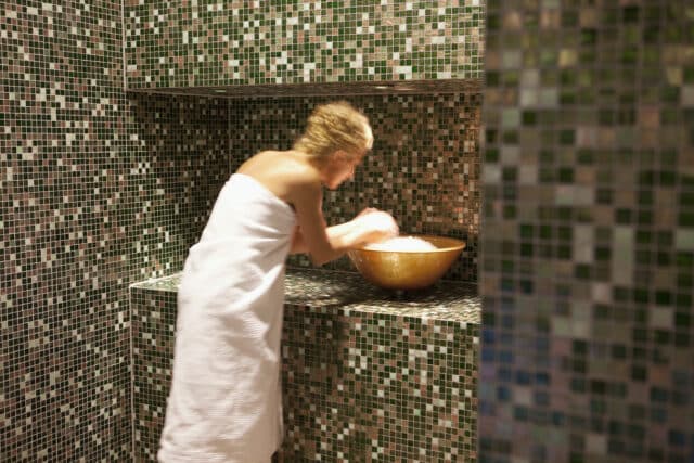 Frau mit Handtuch bekleidet greift in eine Schüssel voller Eis im modern gestalteten Saunabereich der Therme Wien.