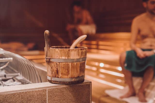 Kuebel für Aufguss in der Sauna. Zwei Herren sitzen im Hintergrund in der Sauna der Therme Wien.