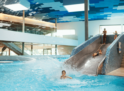 Kinder rutschen ueber eine Wassertusche in der Therme Wien ins Wasser.