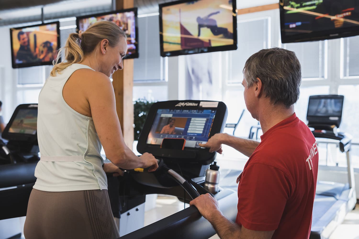 Trainer beraet Frau, die auf einem Laufband steht, bei einem Probetraining Therme Wien Fitness.