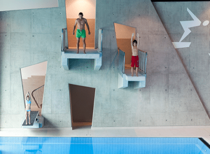 Ein Mann und zwei Kinder springen von unterschiedlich hohen Springtuermen in der Therme Wien.