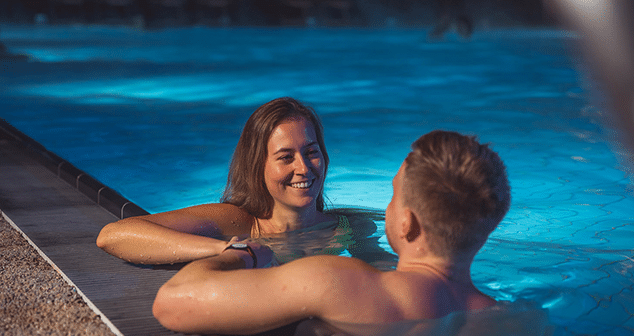 Junges paar liegt entspannt an einem Sommerabend outdoor in einem Becken der Therme Wien.