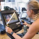 Blonde Frau beim Cardio Training in der Therme Wien Fitness. Beide Haende sind auf den Griffen.