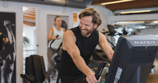 Junger Mann sitzt auf dem Tainingsgeraet und macht Cardiotraining in der Therme Wien Fitness.