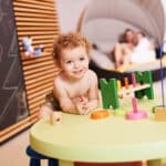 Kleiner Junge in Badehose beim Spielen an einem Tisch mikt Spielsachen im Kinderbereich der Therme Wien.