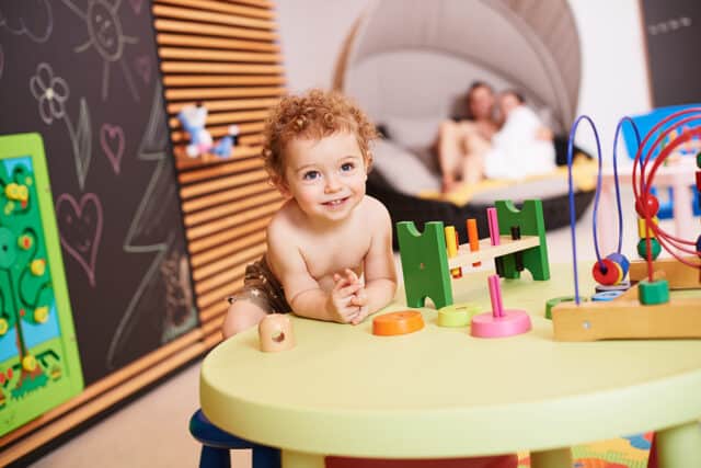 Kleiner Junge in Badehose beim Spielen an einem Tisch mikt Spielsachen im Kinderbereich der Therme Wien.