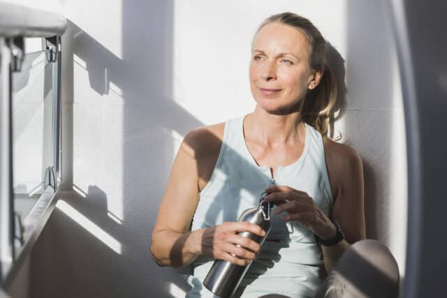 Frau atmet durch in der Pause beim Fitnesstraining und trinkt aus der Trinkflasche