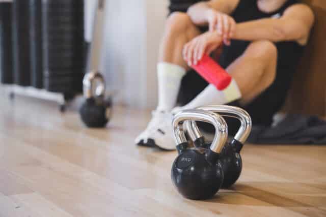 8 Kg Kettlebells beim Fitnesstrainign der Therme Wien Fitness. Im Hintergrund sitzt ein Mann und atmet durch.