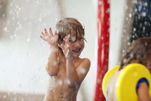 Kleiner Junge spielt im Springbrunnen im Kinderbereich der Therme Wien.