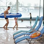 Vater und zwei Kinder gehen am Beckenrand mit Luftmatratze in der Therme Wien.