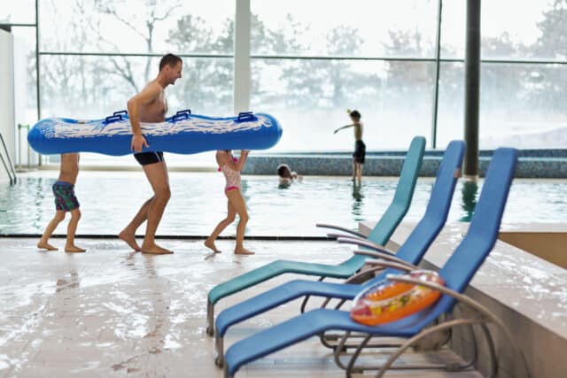 Vater und zwei Kinder gehen am Beckenrand mit Luftmatratze in der Therme Wien.