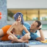 Vater und Sohn liegen entspannt in der Therme Wien. Der Sohn laechelt in die Kamera.