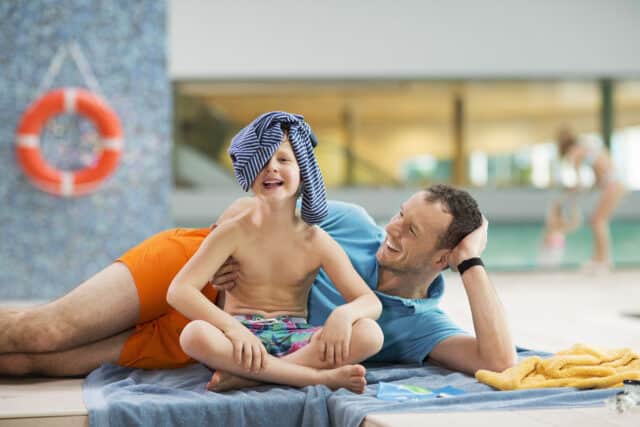 Vater und Sohn liegen entspannt in der Therme Wien. Der Sohn laechelt in die Kamera.