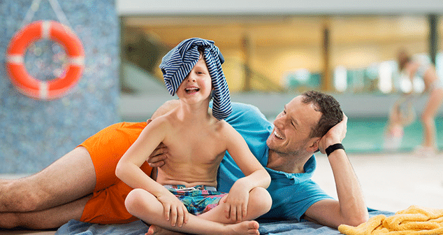 Vater und Sohn liegen entspannt in der Therme Wien. Der Sohn laechelt in die Kamera.