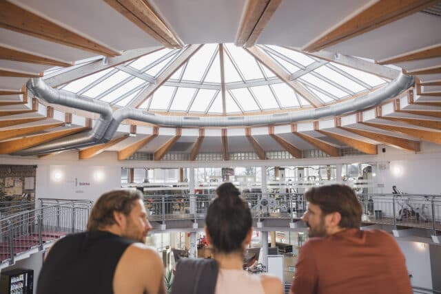 Zwei Maenner und eine junge Frau stehen in der Therme Wien Fitness und schauen beim Aufgang herunter.