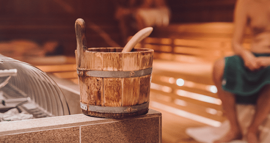 Kuebel für Aufguss in der Sauna. Zwei Herren sitzen im Hintergrund in der Sauna der Therme Wien.