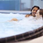 Zwei Freundinnen entspannen und lachen im Sprudelbecken in der Therme Wien.