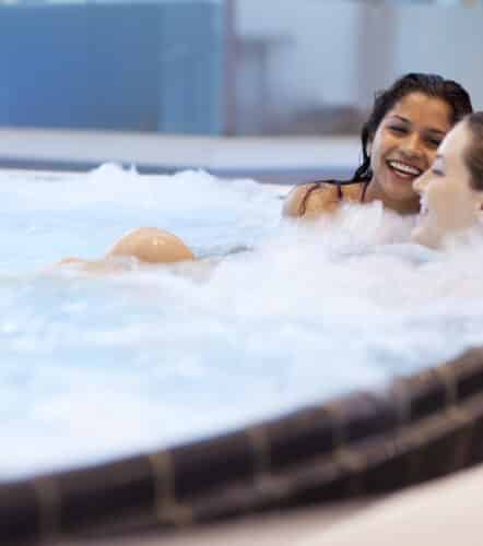 Zwei Freundinnen entspannen und lachen im Sprudelbecken in der Therme Wien.