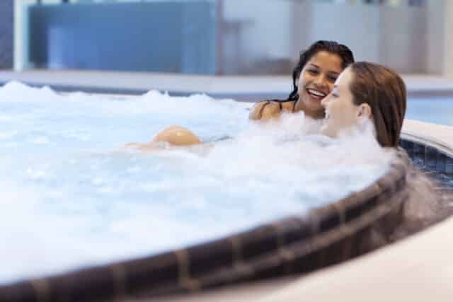 Zwei Freundinnen entspannen und lachen im Sprudelbecken in der Therme Wien.