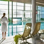 Frau im Bademantel steht am Beckenrand der Thermenlandschaft in der Therme Wien.