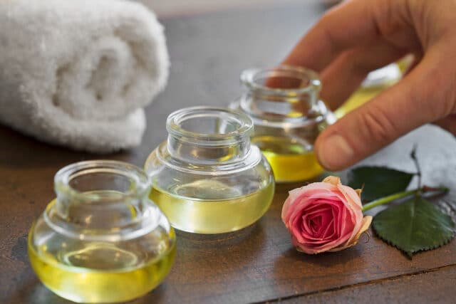 Hand greift nach Aromaoel fuer aroma massage 50 minuten. Auf dem Tisch liegen auch eine Rose und ein Handtuch.