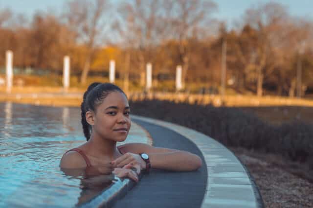 Frau entspannt im Herbst am Beckenrand eines Beckens im Aussenbereich der Therme Wien.