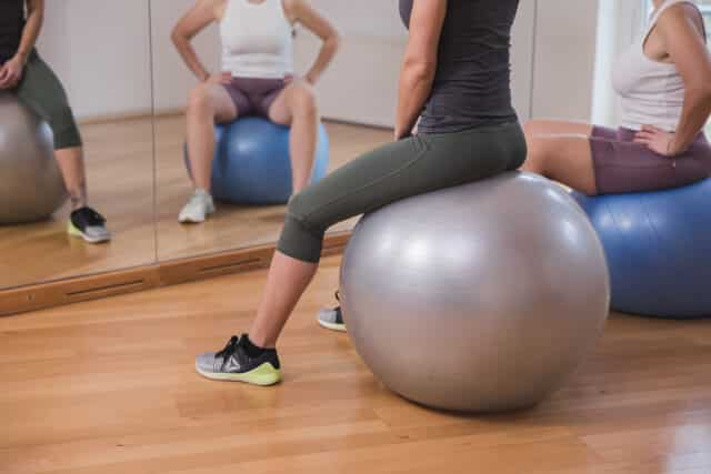 Frau sitzt am Gymnastikball und macht Uebungen fuer ihre Fitness.