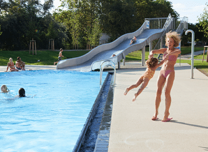 Mutter spielt mit ihrem Kind am Beckenrand des Aussenbereichs der Therme Wien.