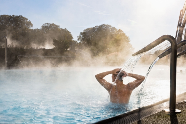 Mann steht unter dem Relax Lounge Wasserschwall im Aussenbecken.