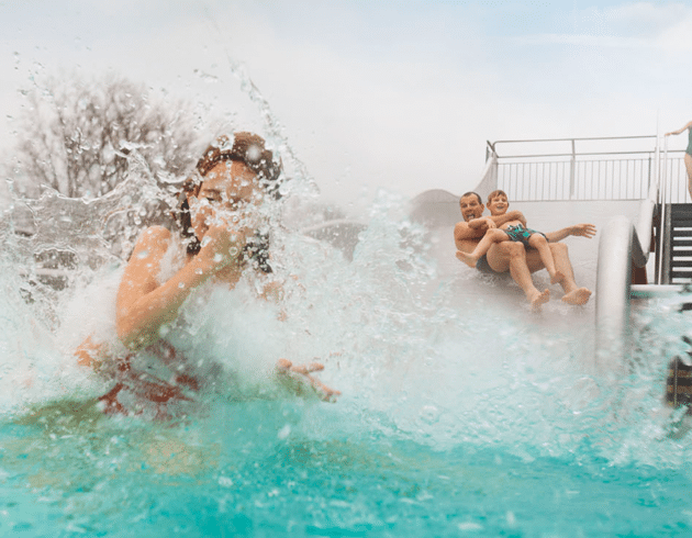 Tochter, Vater und Sohn rutschen eine Wasserrutsche hinunter im Aussenbereich der Therme Wien.