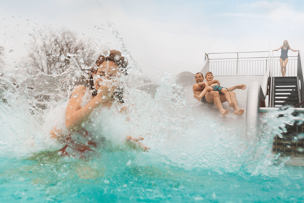 Tochter, Vater und Sohn rutschen eine Wasserrutsche hinunter im Aussenbereich der Therme Wien.