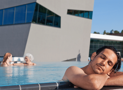 Mann lehnt im Sommer entspannt am Beckenrand des Thermalbeckens der Therme Wien.